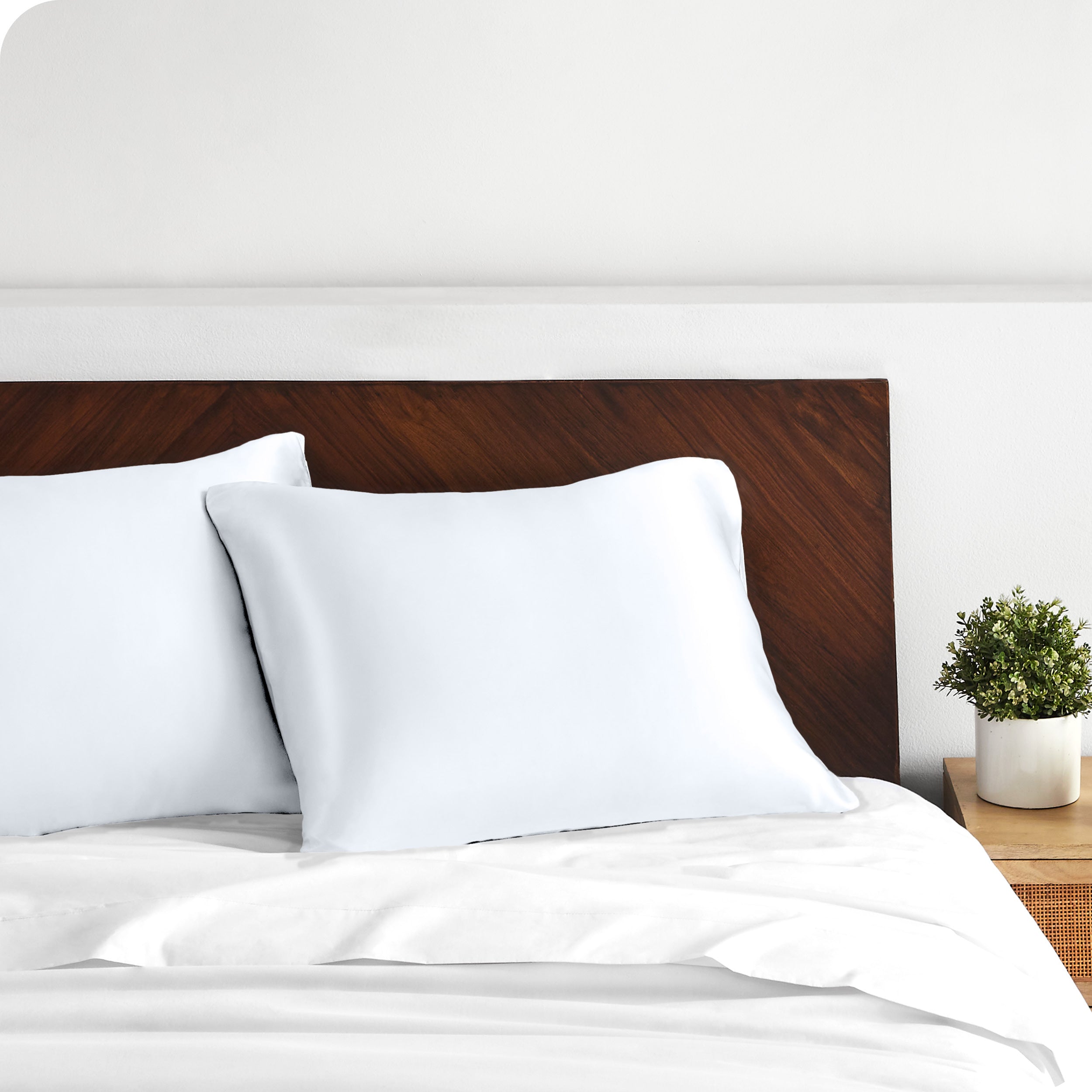 Two satin pillowcases on pillows against a wooden headboard