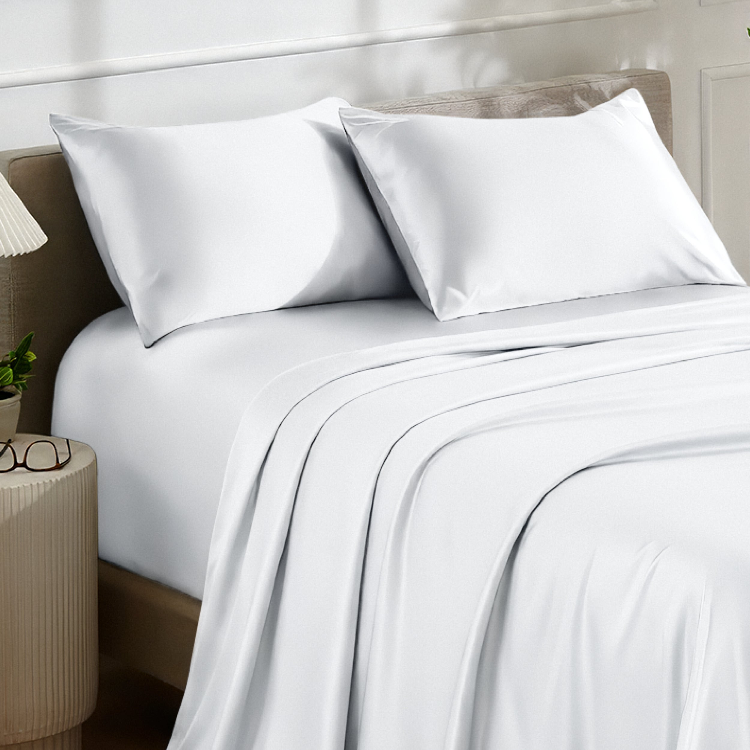 Satin bedding set on a bed with a nightstand and lamp in the background.
