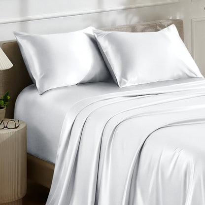 Satin bedding set on a bed with a nightstand and lamp in the background.