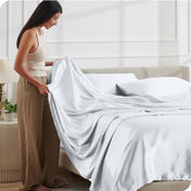 A woman is putting satin sheets on a bed