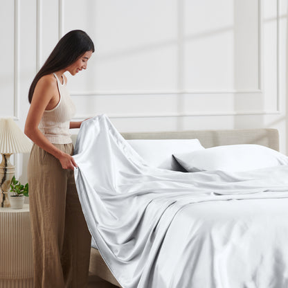Woman arranging satin bedding on a bed in a bright bedroom.