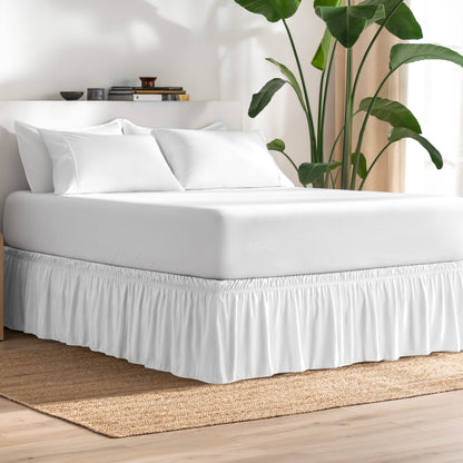 Bed with bed skirt, white bedding, and a plant in a room.