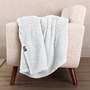 Faux shearling blanket draped over a beige armchair with a wooden base.