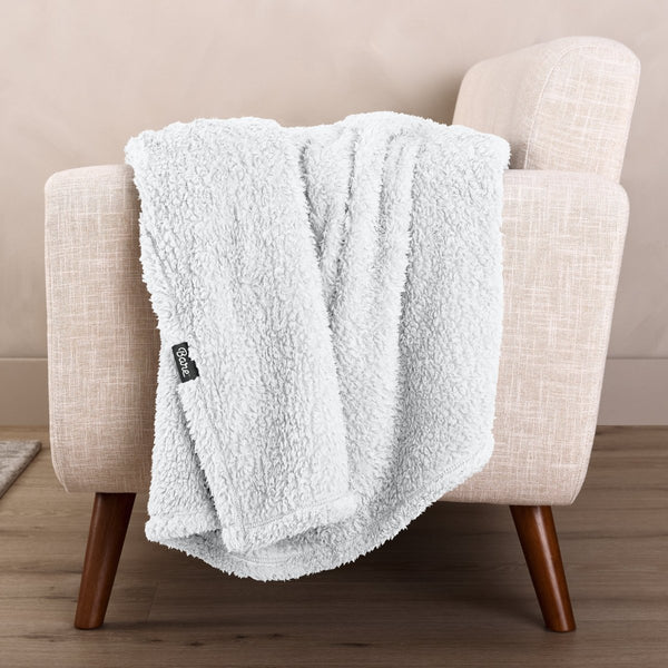 Faux shearling blanket draped over a beige armchair with a wooden base.