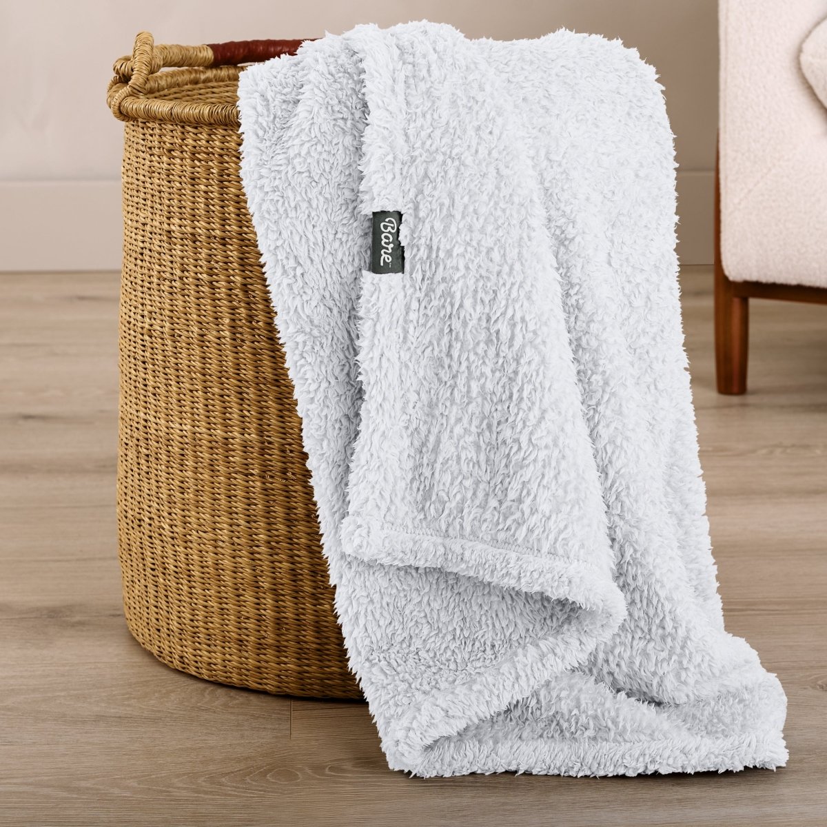 Fluffy blanket draped over a woven basket on a wooden floor.