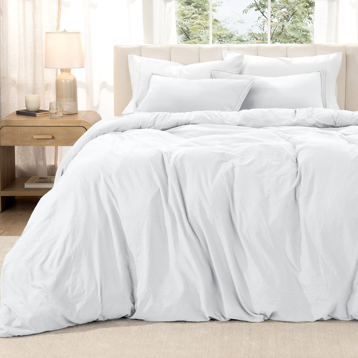 Washed duvet set on a bed in a bright bedroom with a lamp and window.