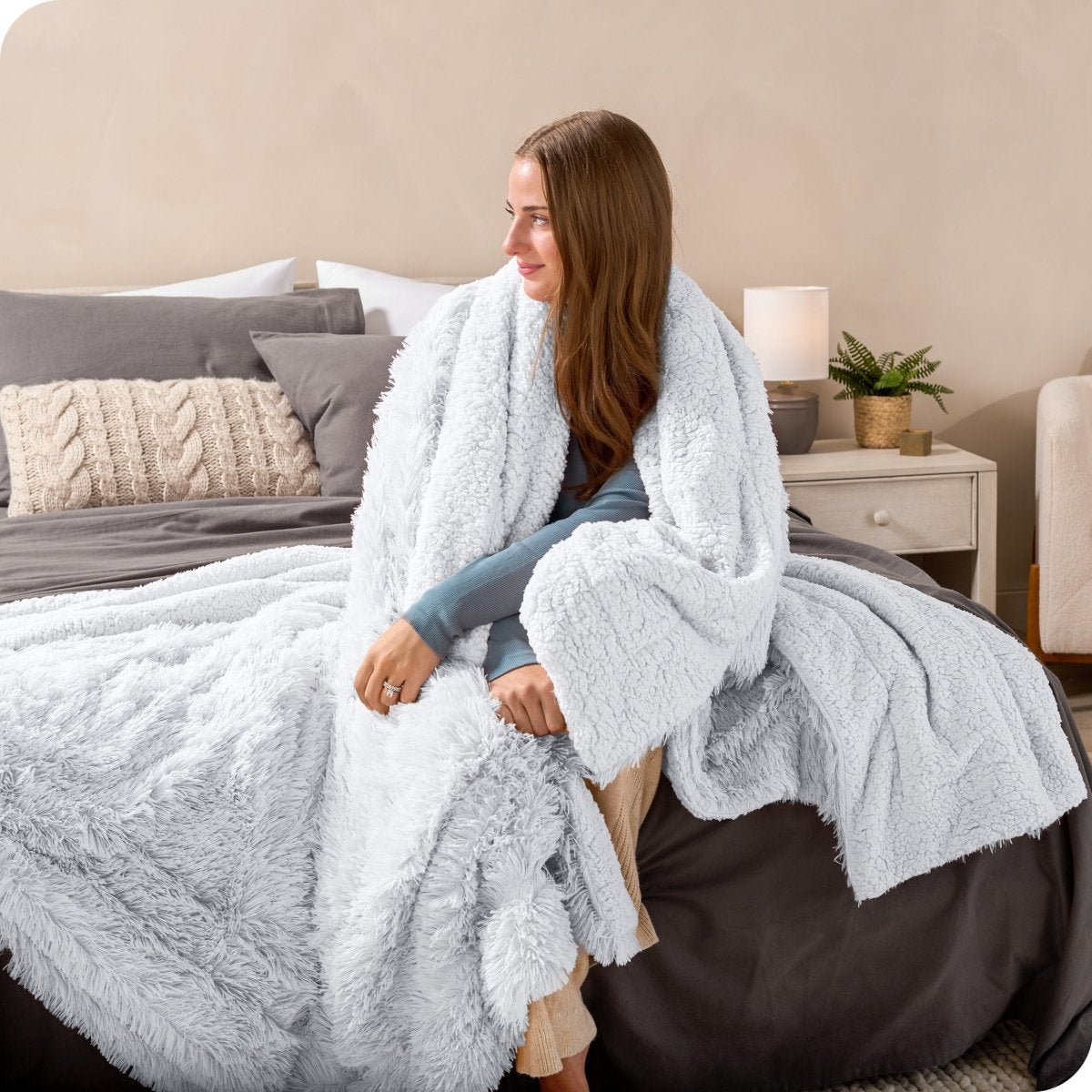 A woman sitting on the end of a bed with a shaggy blanket wrapped around her