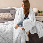 Fluffy blanket draped over a woman sitting on the end of a bed