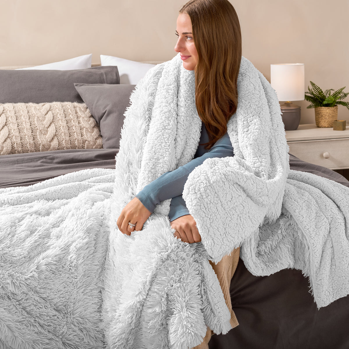 Fluffy blanket draped over a woman sitting on the end of a bed