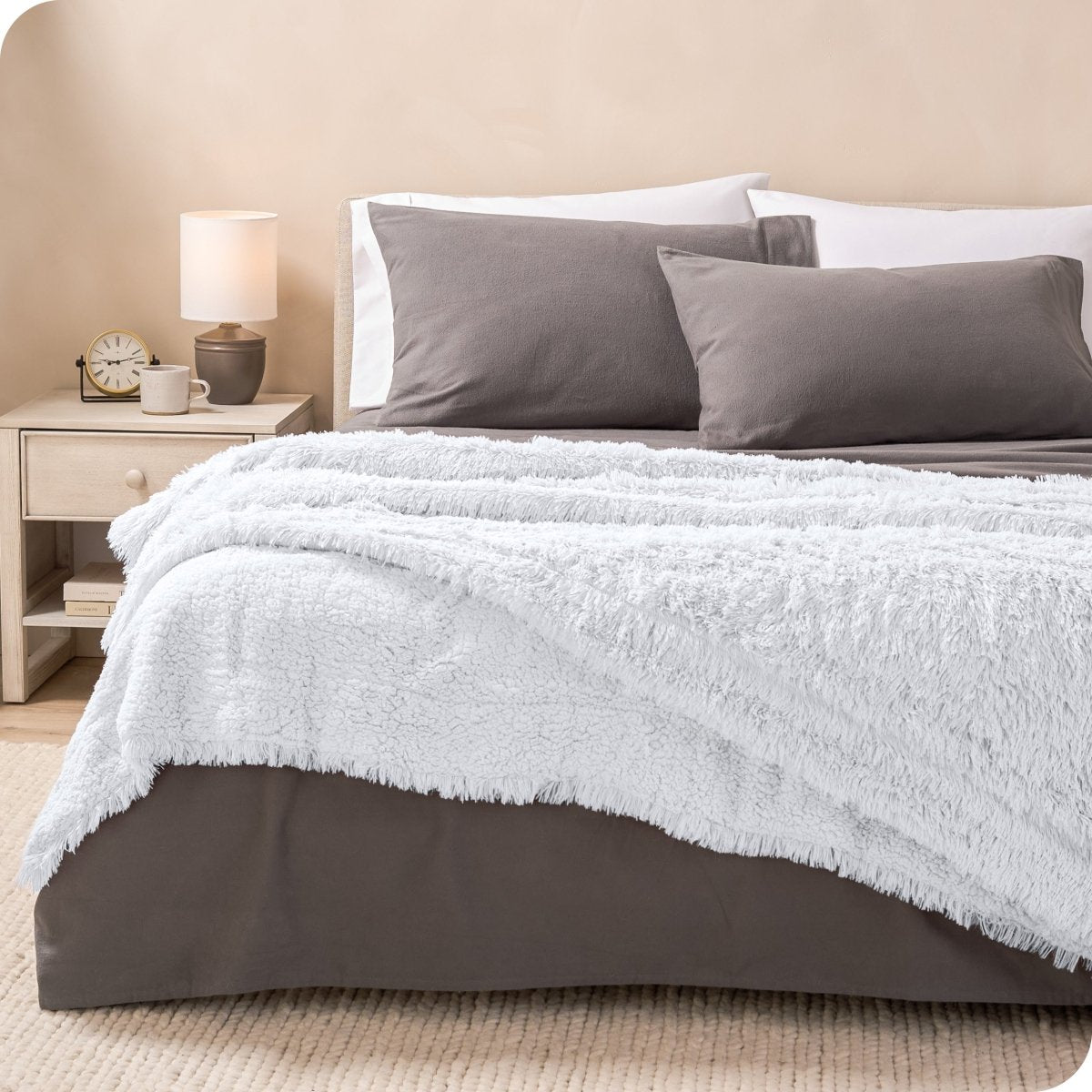 A woman sitting on the end of a bed with a shaggy blanket wrapped around her