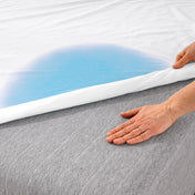 A woman is pressing her hand on a mattress which is partially covered with a mattress protector