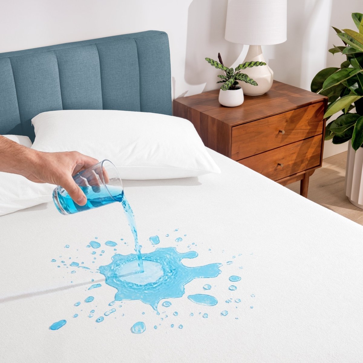Person pouring liquid onto a white mattress protector in a bedroom setting.