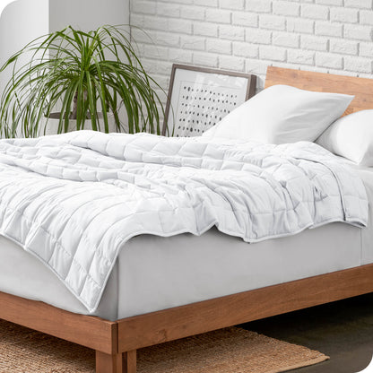 Weighted blanket on a bed with white pillows and a wooden headboard in a room with a plant and brick wall.