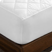 Close up of the corner of a bed with a white mattress pad on it