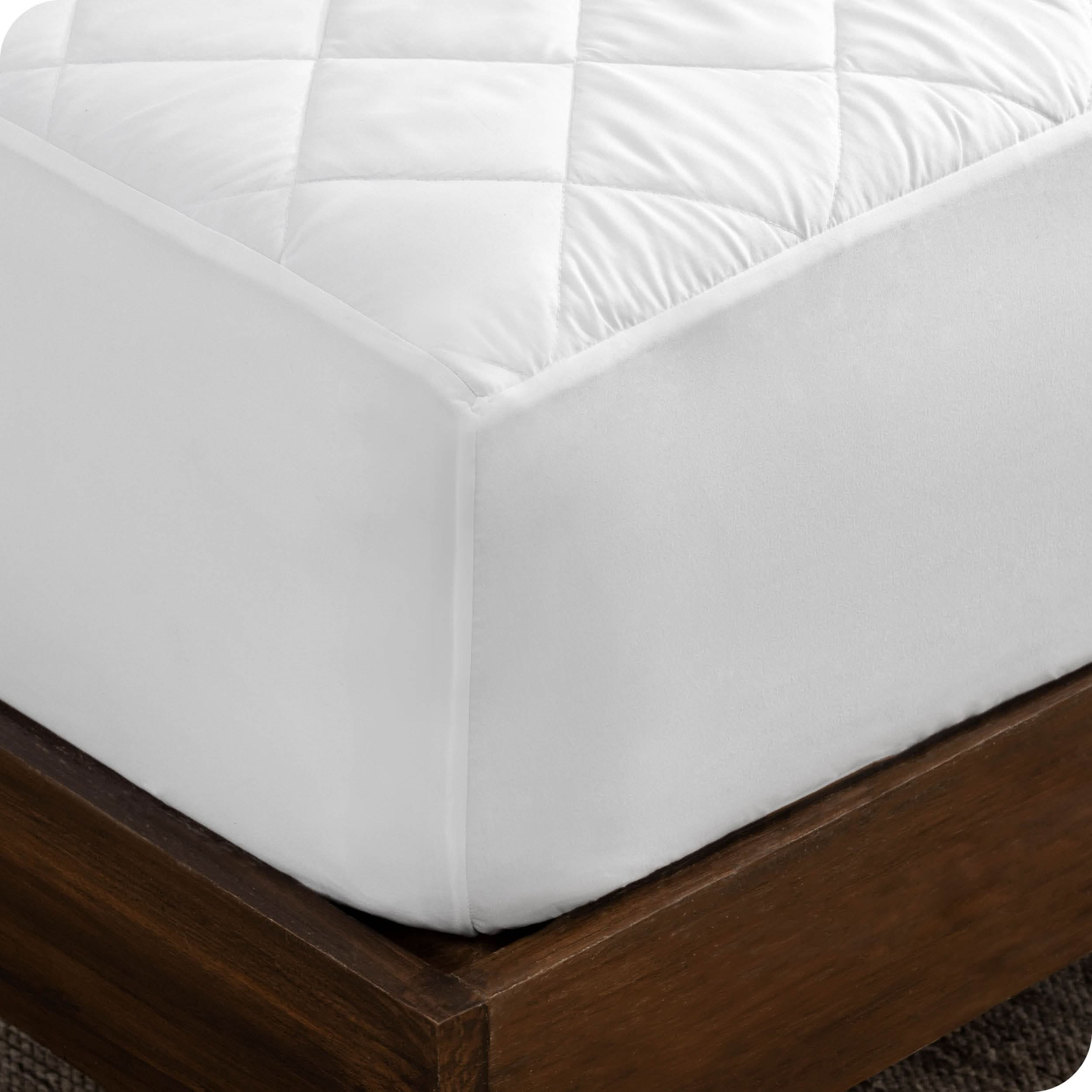 Close up of the corner of a bed with a white mattress pad on it