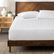 A mattress pad on a bed with white pillowcases on pillows set on top near the headboard