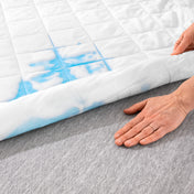 Close up of a hand on a mattress with a mattress pad on part of the mattress