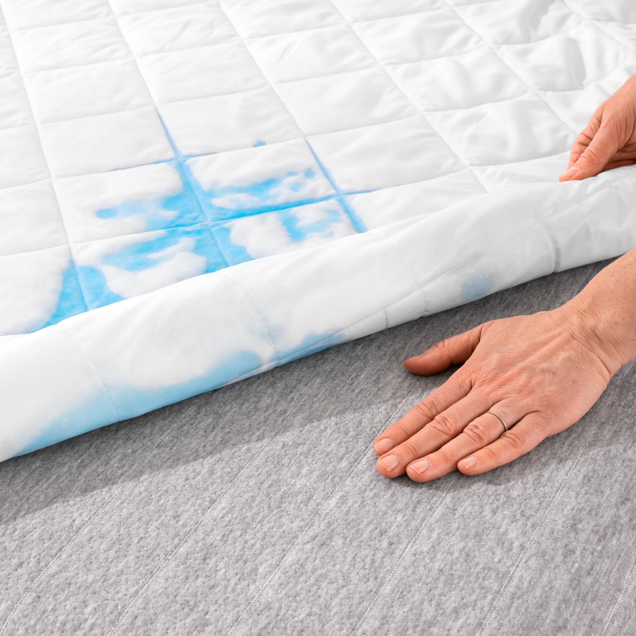 Close up of a hand on a mattress with a mattress pad on part of the mattress