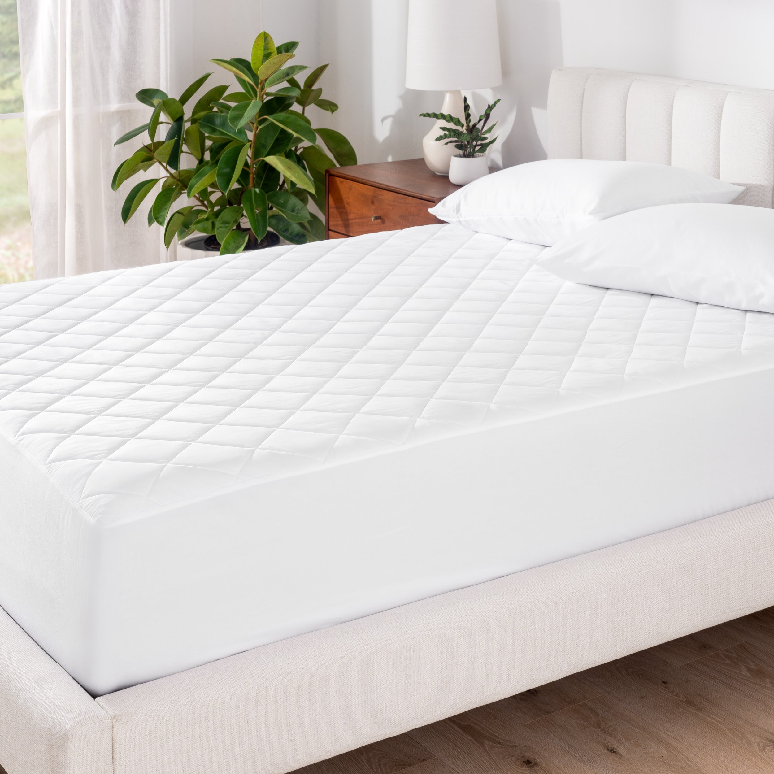 A mattress pad on a bed with white pillowcases on pillows set on top near the headboard