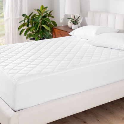 A mattress pad on a bed with white pillowcases on pillows set on top near the headboard