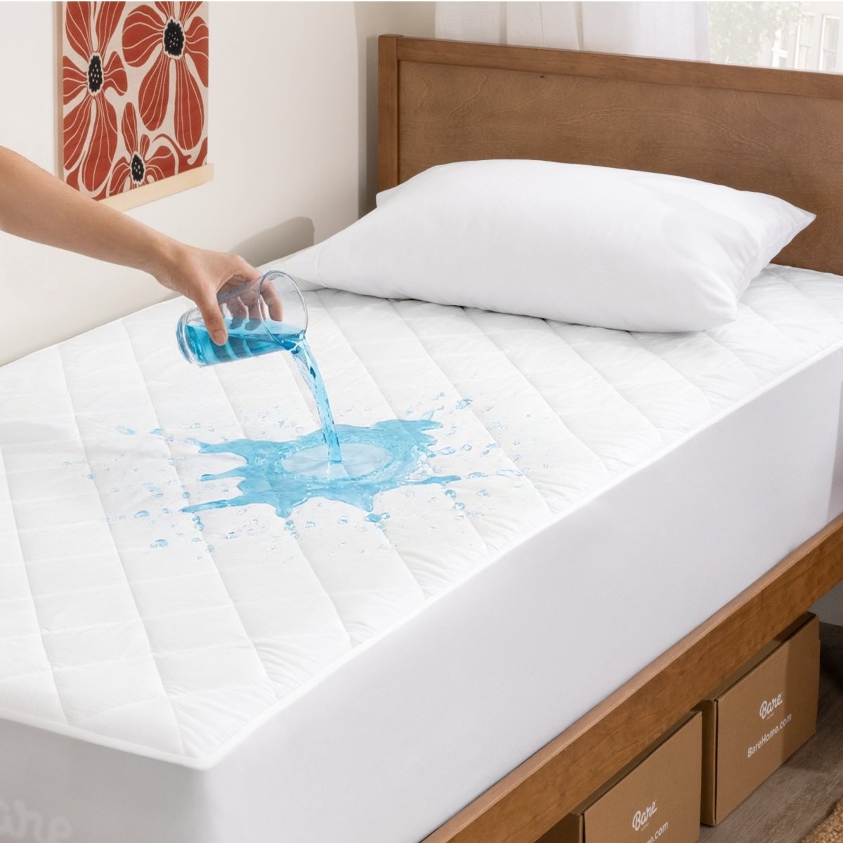 Person pouring blue liquid onto a white mattress pad on a bed.
