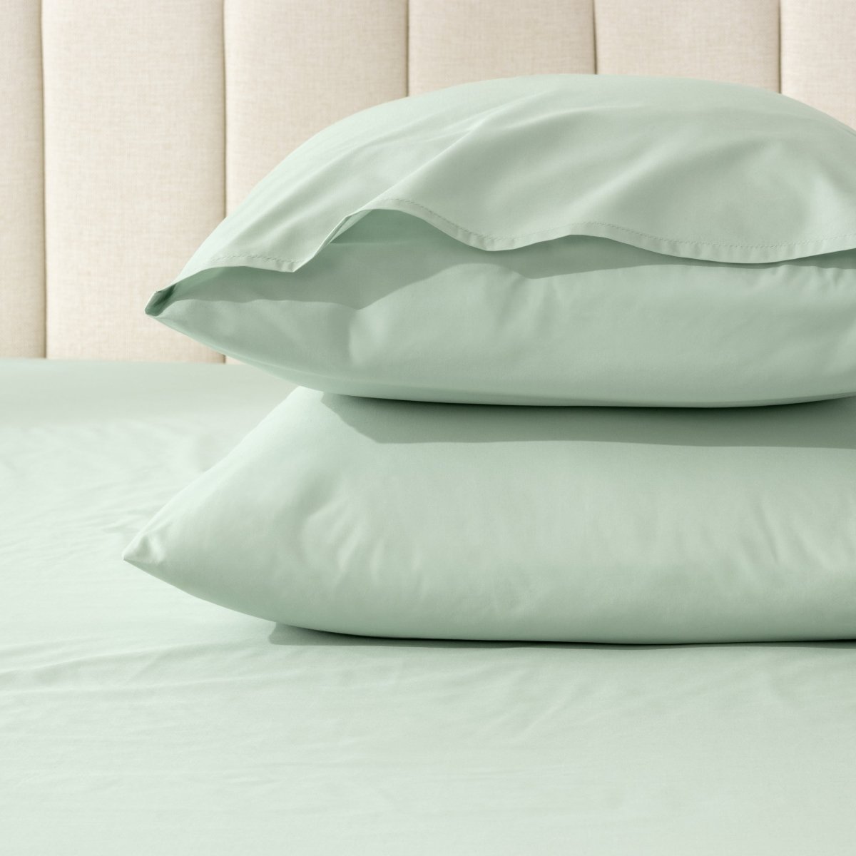 Two pillows stacked on a bed with percale pillowcases on them