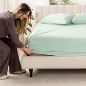 Woman adjusting a fitted sheet on a bed in a bedroom setting