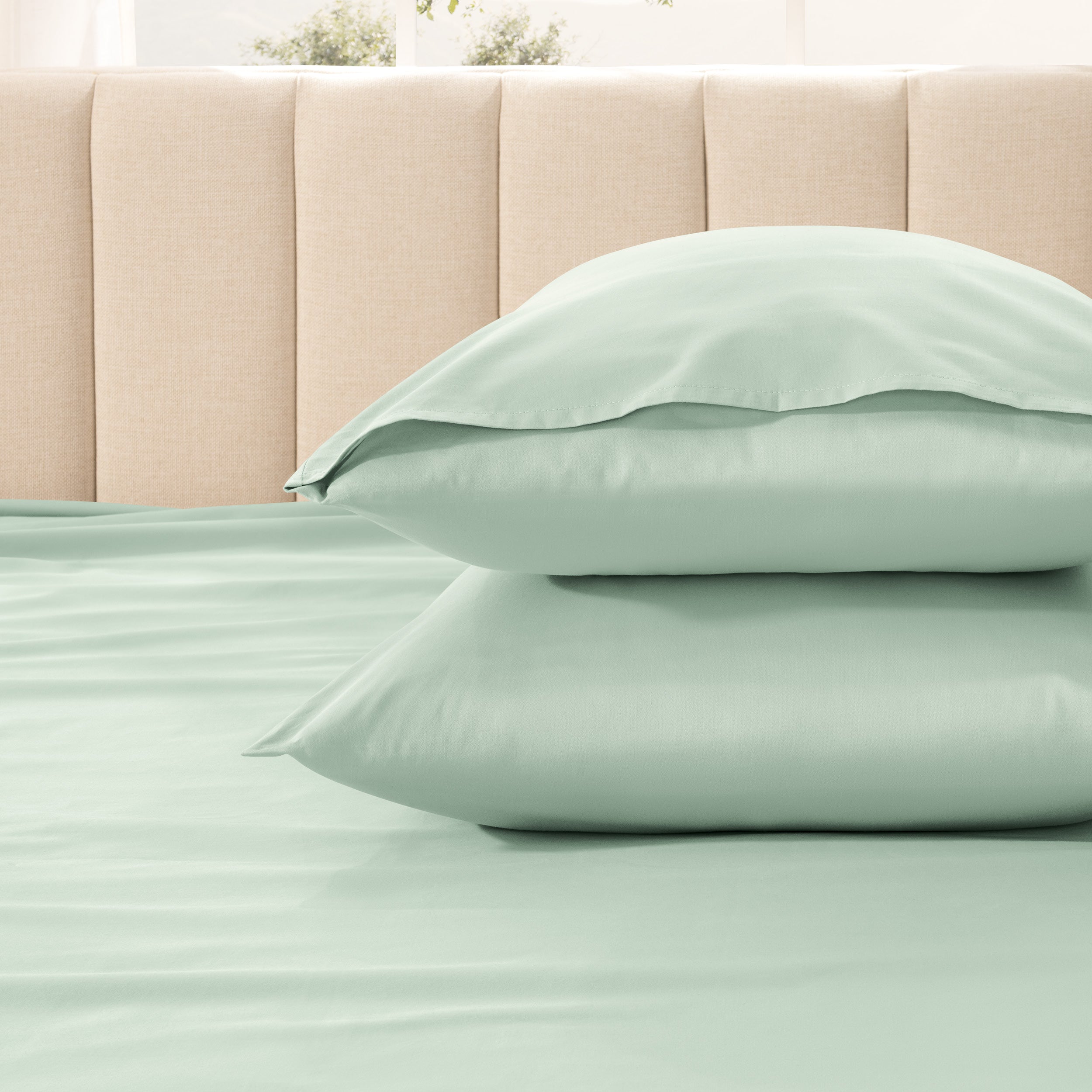 Two pillows stacked on a bed with a beige headboard.