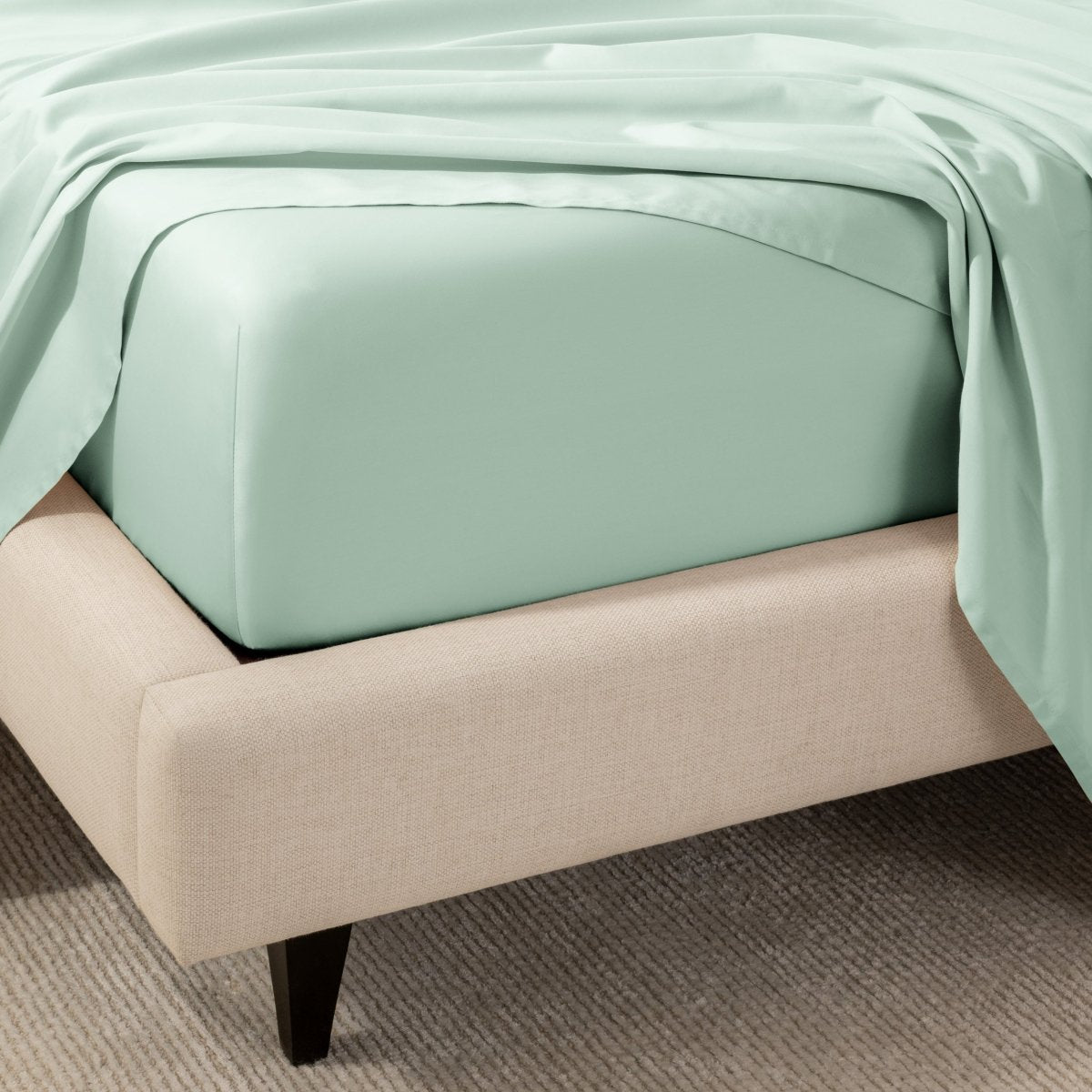 A close-up of the corner of a bed with a fitted sheet and matching flat sheet.
