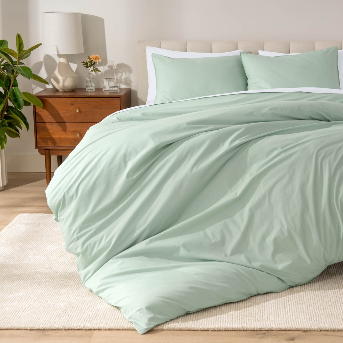 Percale bedding set on a bed in a bedroom with a wooden nightstand and lamp.