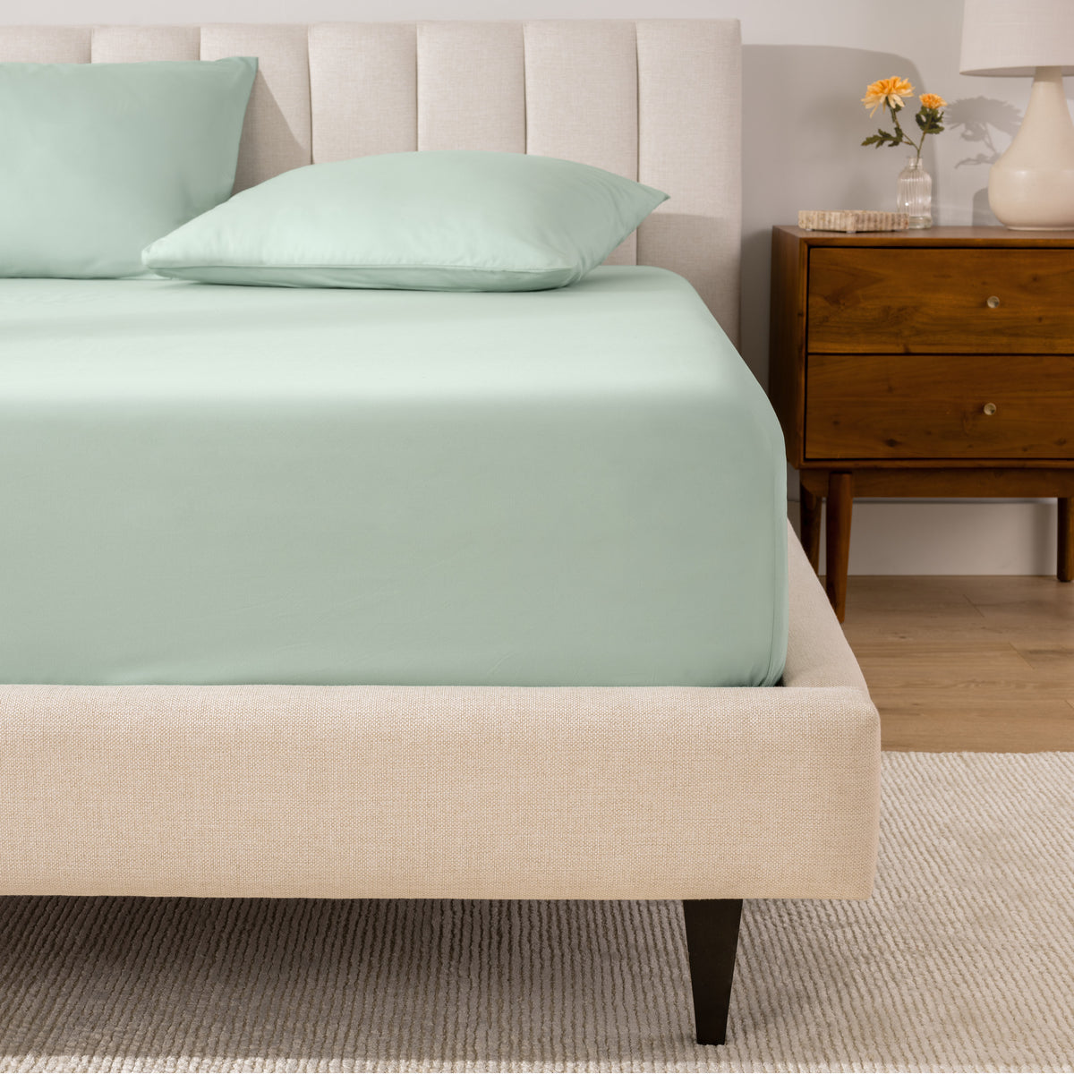 A percale fitted sheet and pillowcases on a bed in a bedroom with a wooden nightstand.
