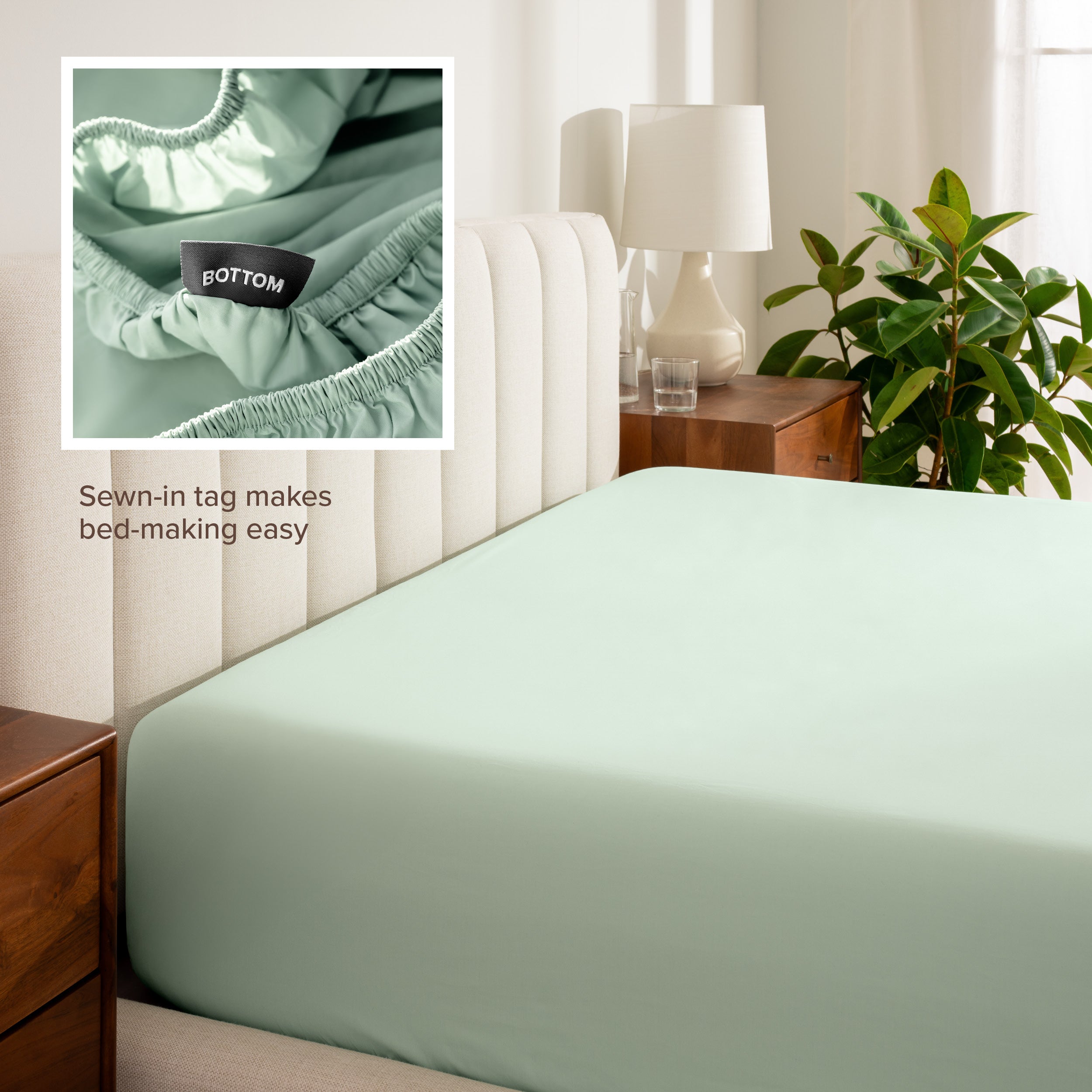 Fitted sheet on a bed with a close-up of a sewn-in tag, nightstand, lamp, and plant in a bedroom setting.
