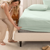 Woman in pajamas adjusting bed sheets on a bed.