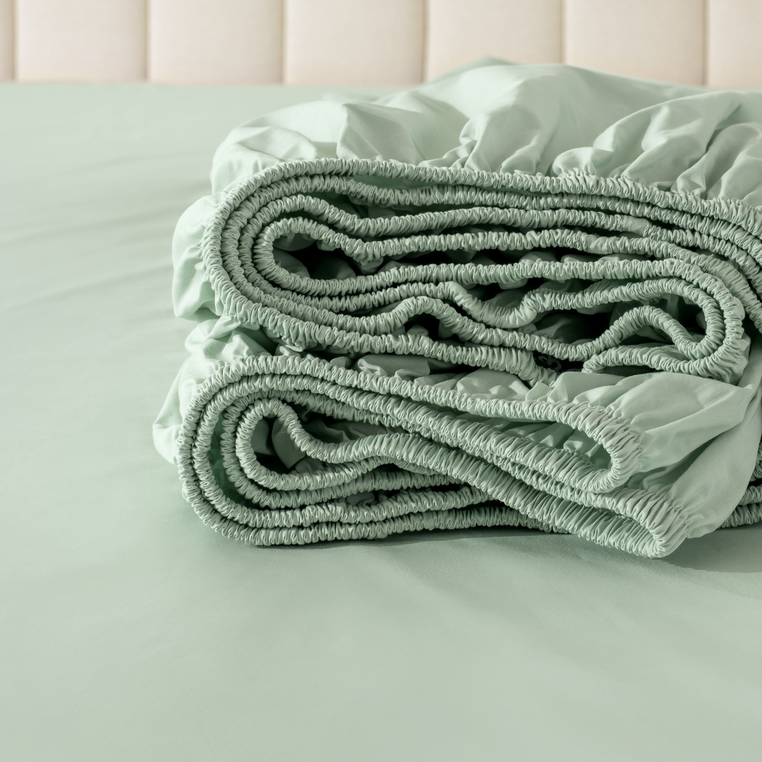 Folded fitted sheet on a bed with a neutral background