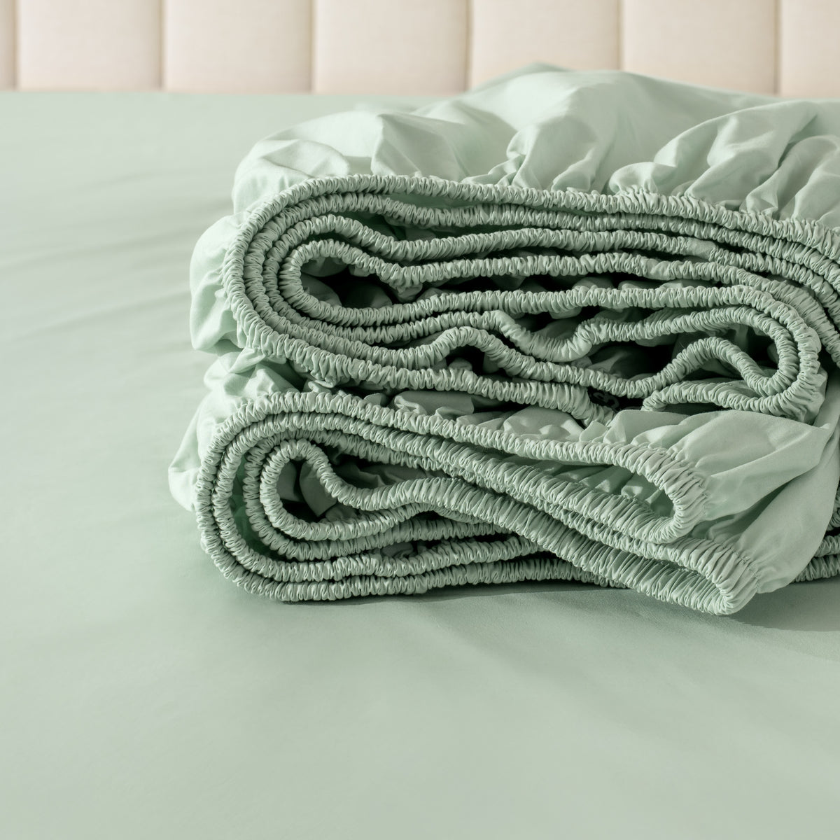 Folded fitted sheet on a bed with a neutral background
