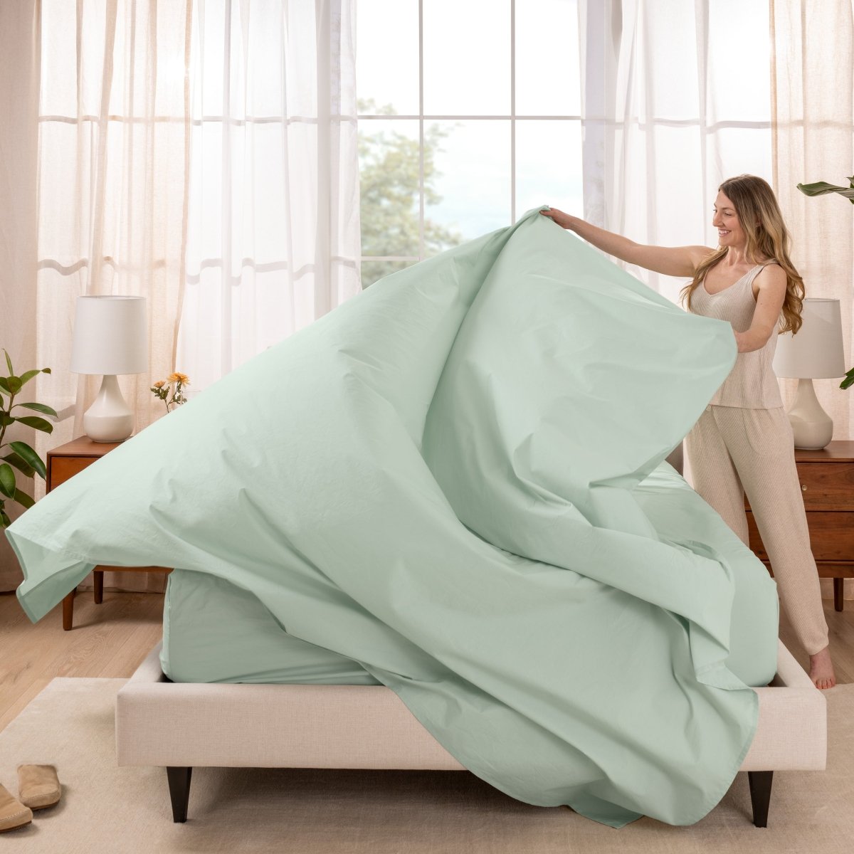 Woman putting a sheet set on a bed in a bright bedroom.