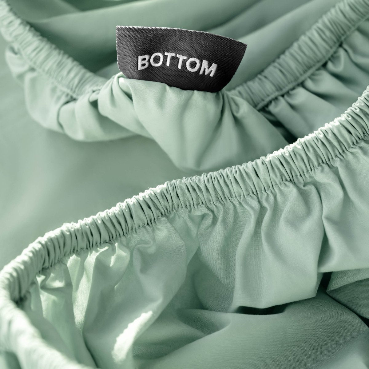 Close-up of a fitted sheet with a black fabric brand label reading BOTTOM.
