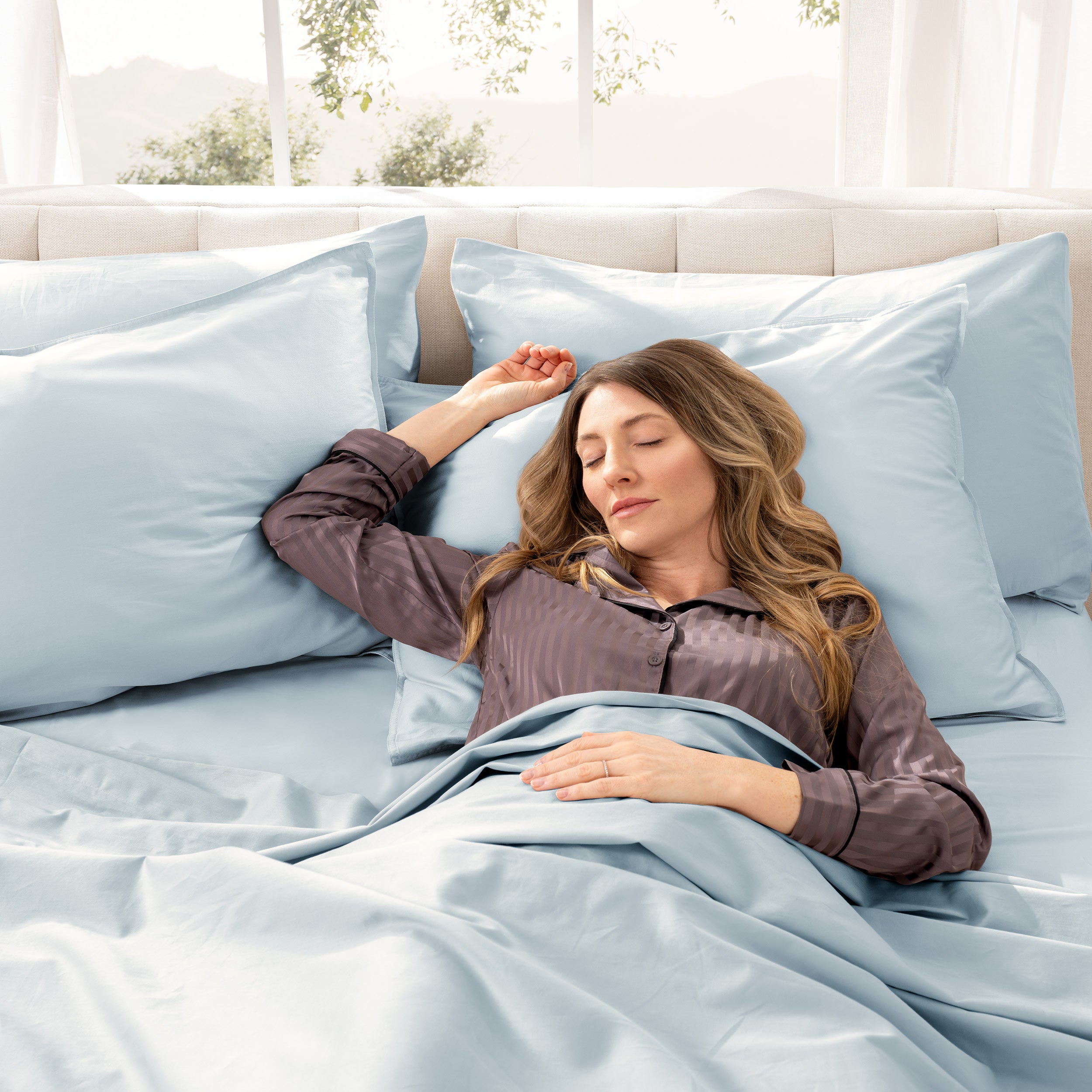 Woman lying in bed with sateen bedding and pillowcases, looking relaxed.