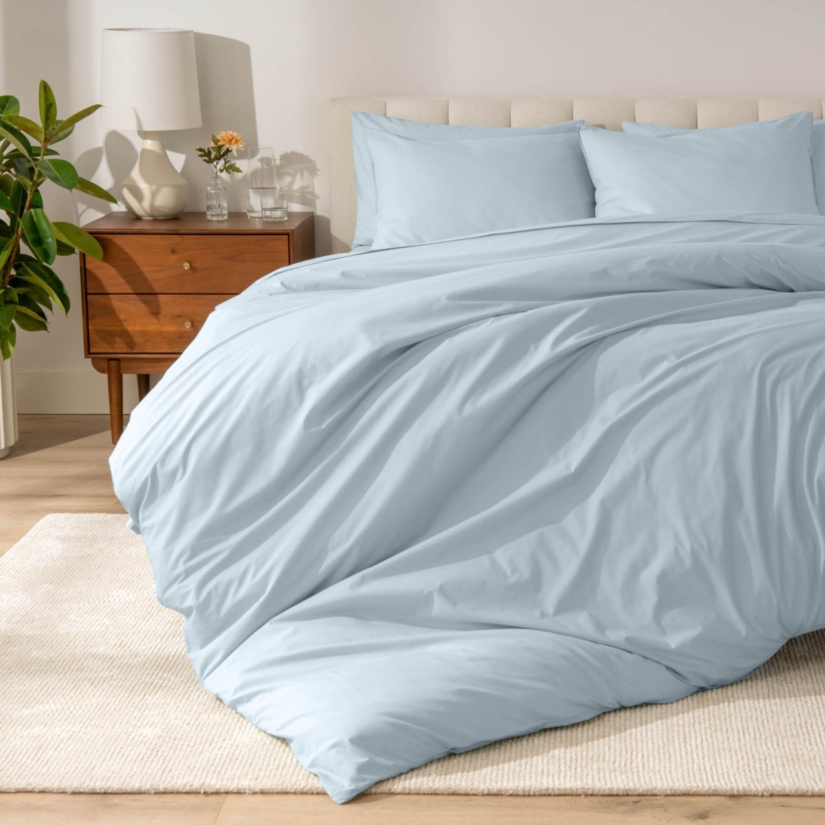 Percale bedding set on a bed in a bedroom with a wooden nightstand and lamp.