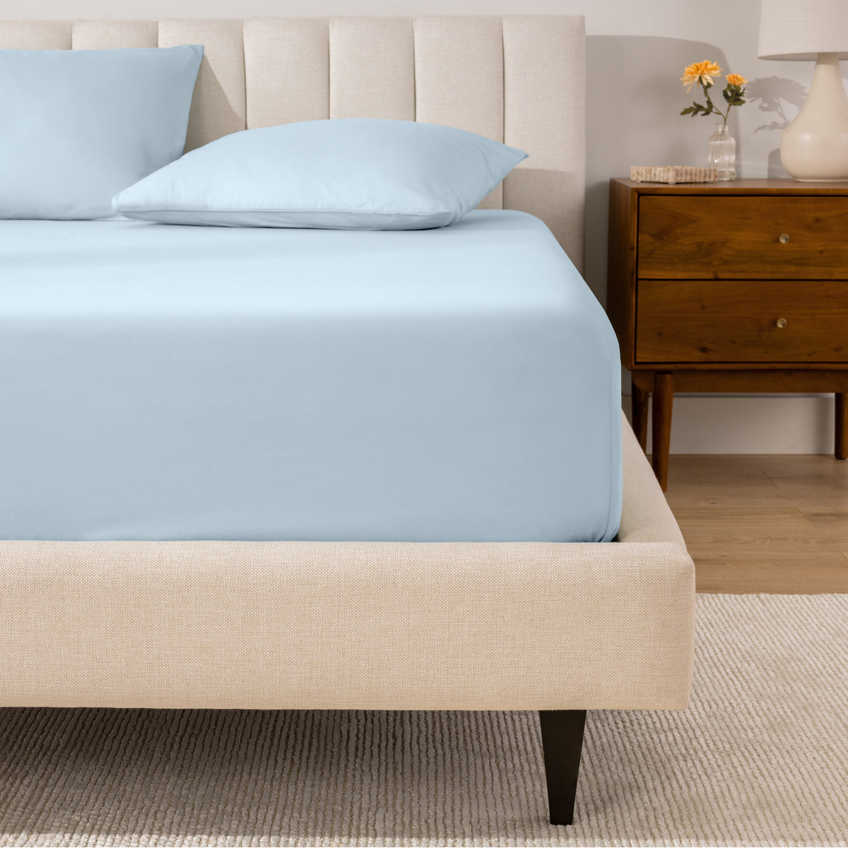 A percale fitted sheet and pillowcases on a bed in a bedroom with a wooden nightstand.