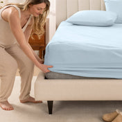 Woman in pajamas adjusting bed sheets on a bed.