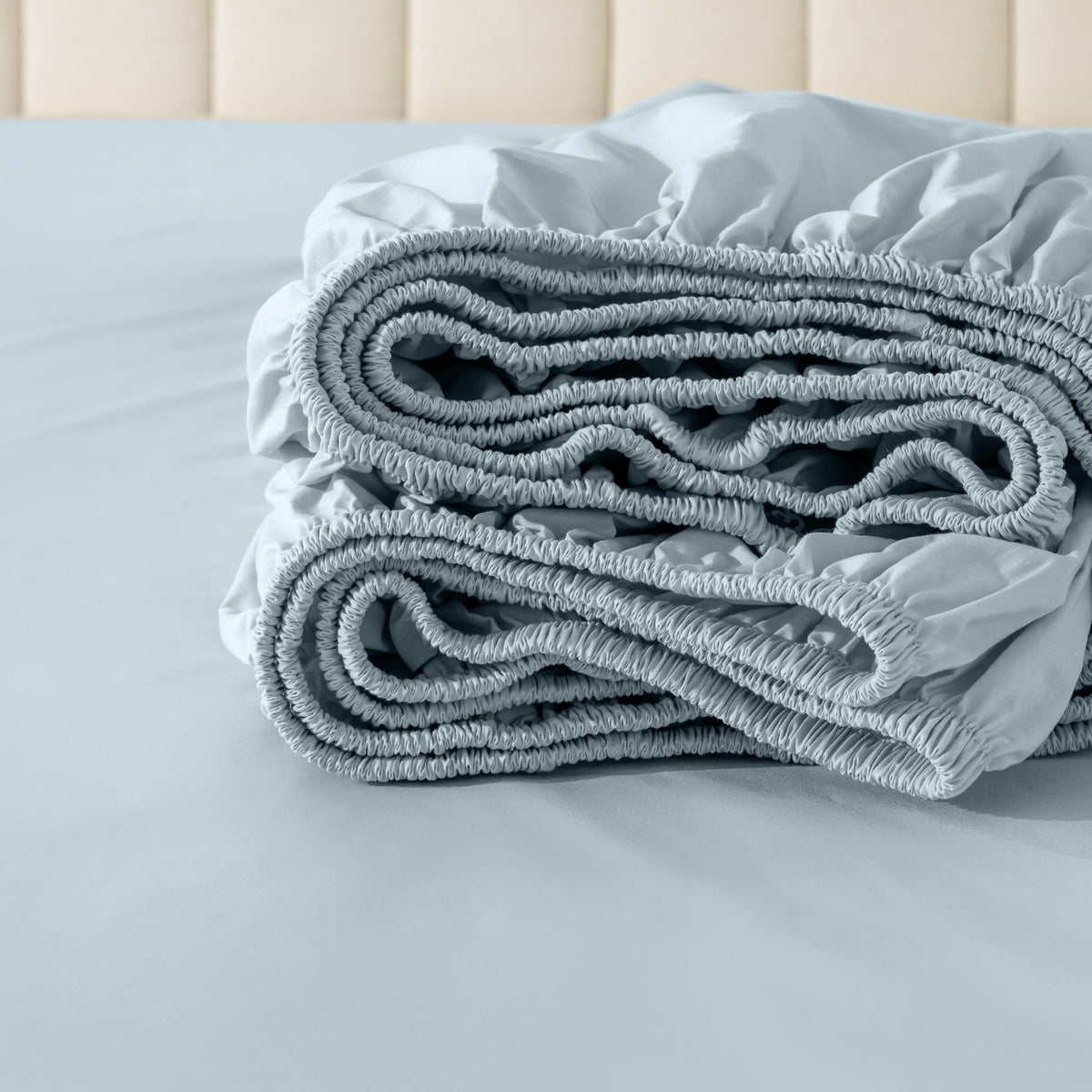 Folded fitted sheet on a bed with a neutral background