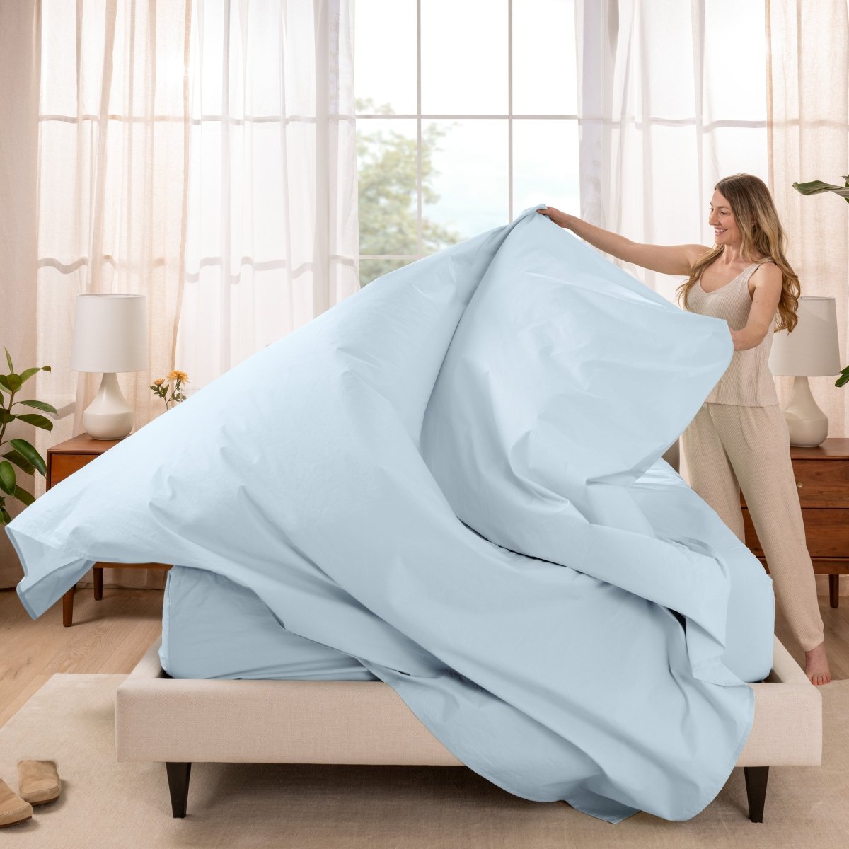 Woman putting a sheet set on a bed in a bright bedroom.