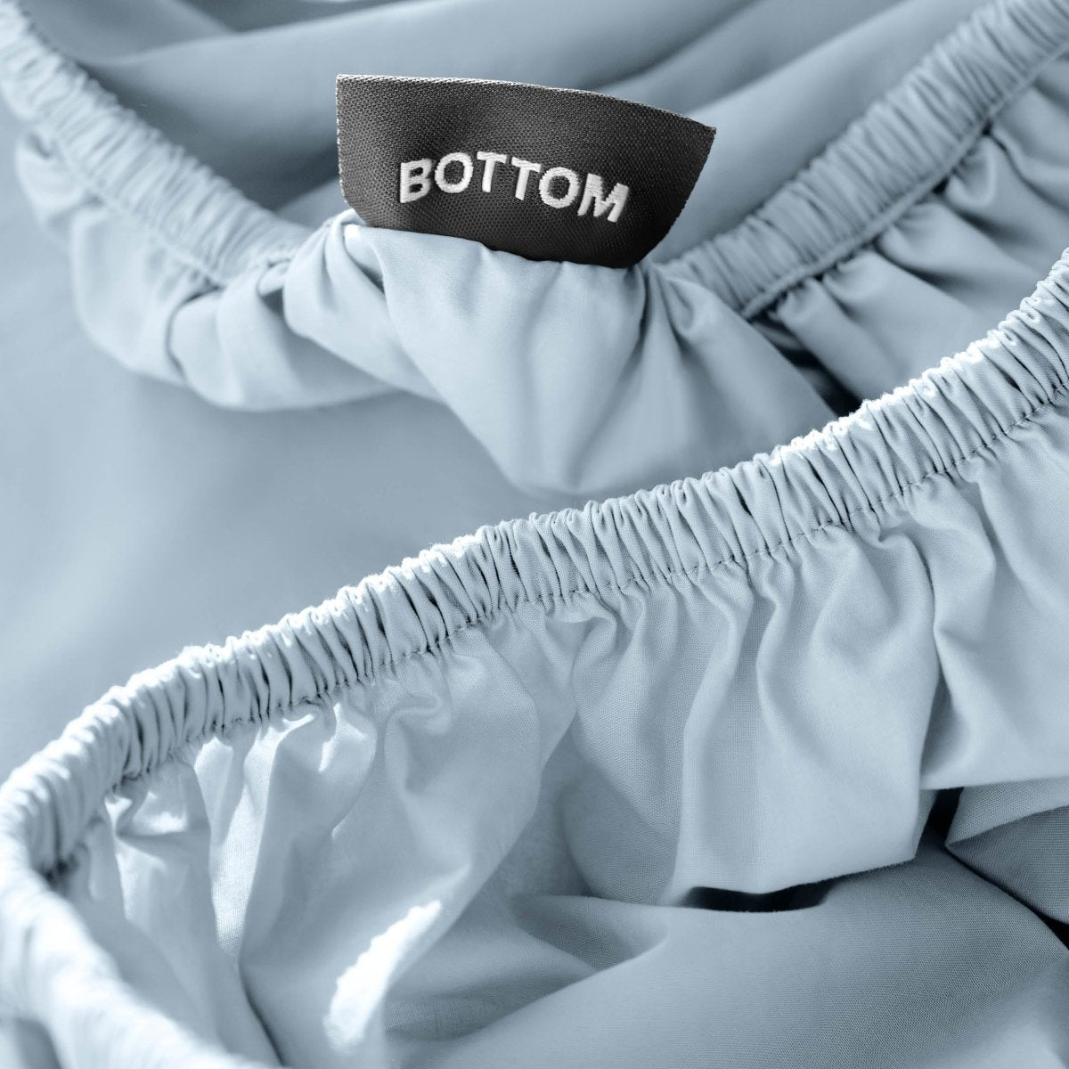 Close-up of a fitted sheet with a black fabric brand label reading BOTTOM.