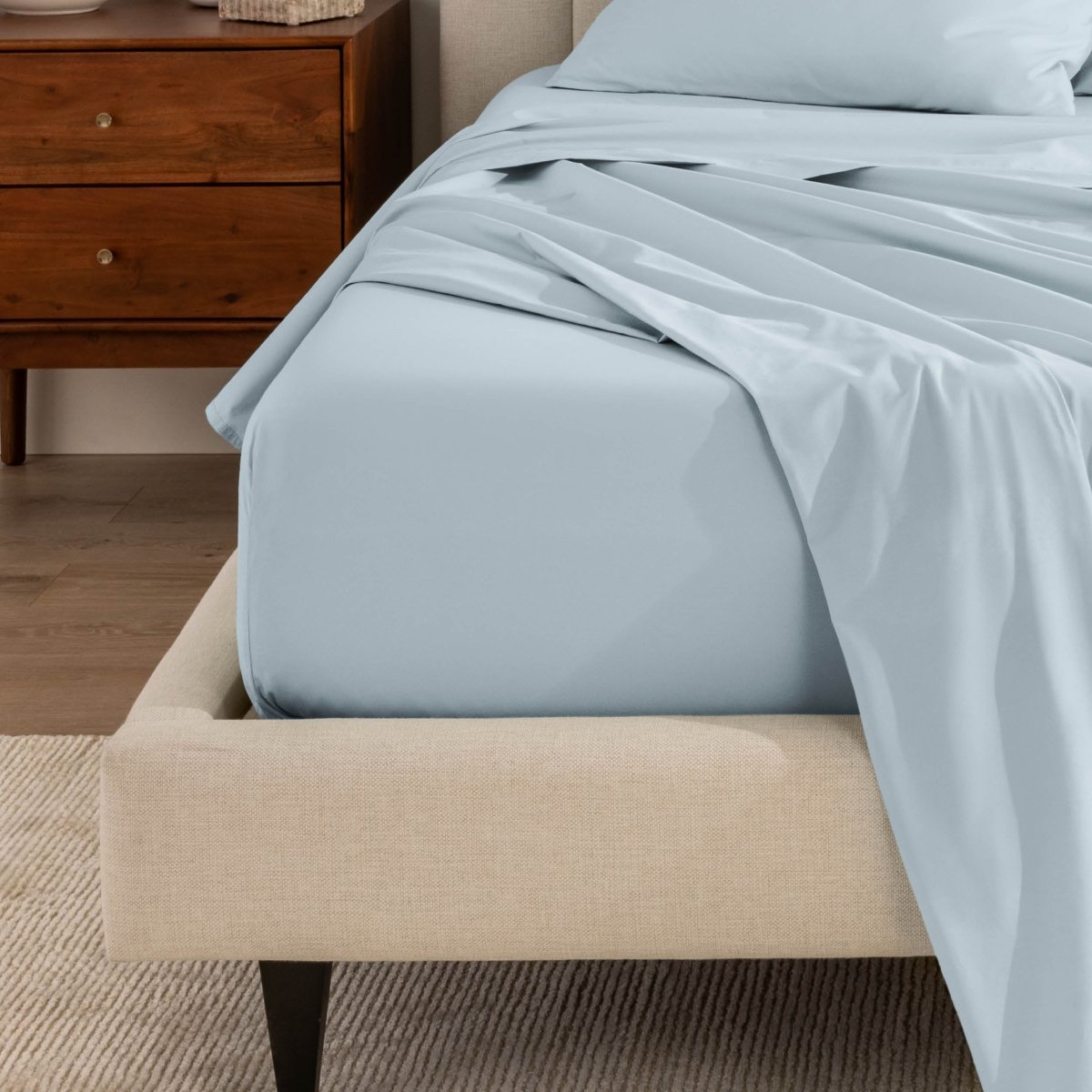 Top sheet and a matching fitted sheet on a bed with a beige bed frame