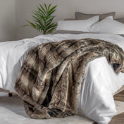 Blanket draped over a bed in a bedroom setting with a nightstand and lamp.