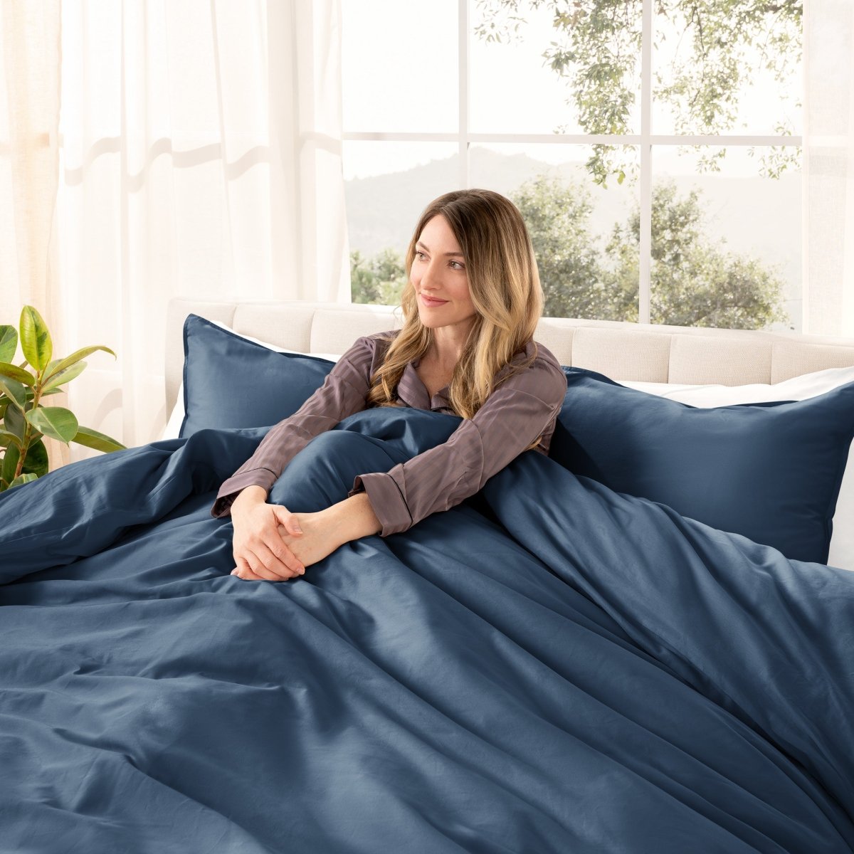 Woman lying on a bed with organic sateen bedding in a bright room with large windows.