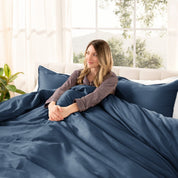 Woman lying on a bed with organic sateen bedding in a bright room with large windows.