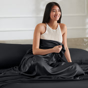 Woman sitting on a bed with a satin sheet over her