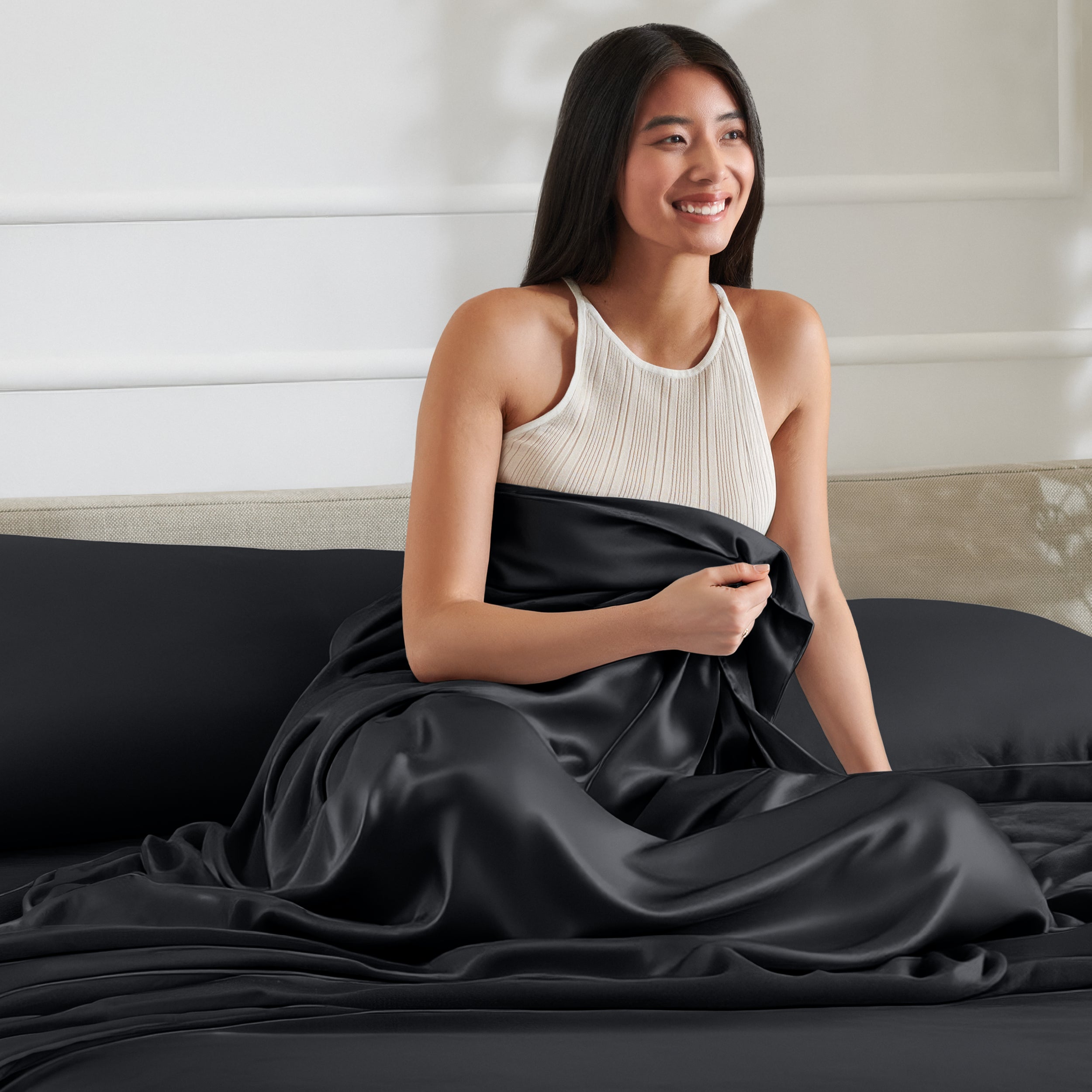 Woman sitting on a bed with a satin sheet over her